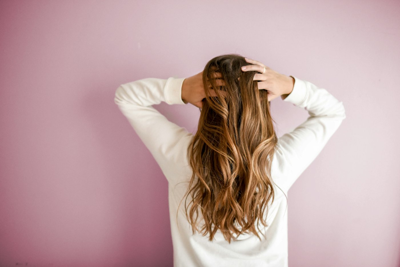 Long glossy honey-brown hair against a pink wall